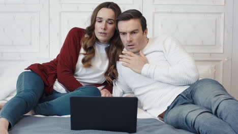 sad couple watching terrible news on computer at home together.