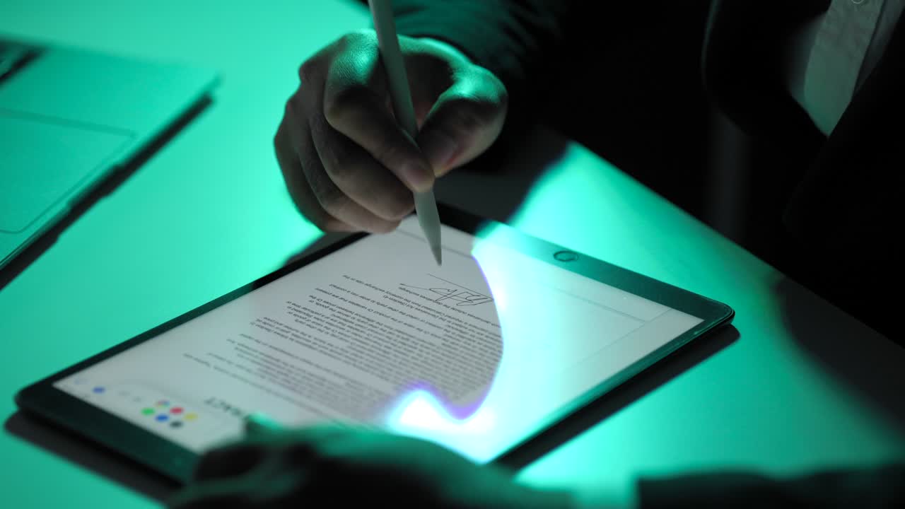 Electronic signature with green light. Businessman signing a business contract with stylus pen on tablet at night. Man signing contract on tablet at office. Business and technology concept.
