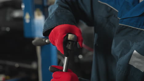 close-up hand view of mechanic loosening nut on car engine wearing red gloves with blurred background of car, mechanical tools, and workshop setting