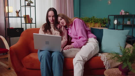 Young-adult-women-couple-looking-at-laptop-notebook-screen-making-online-shopping-purchase-at-home