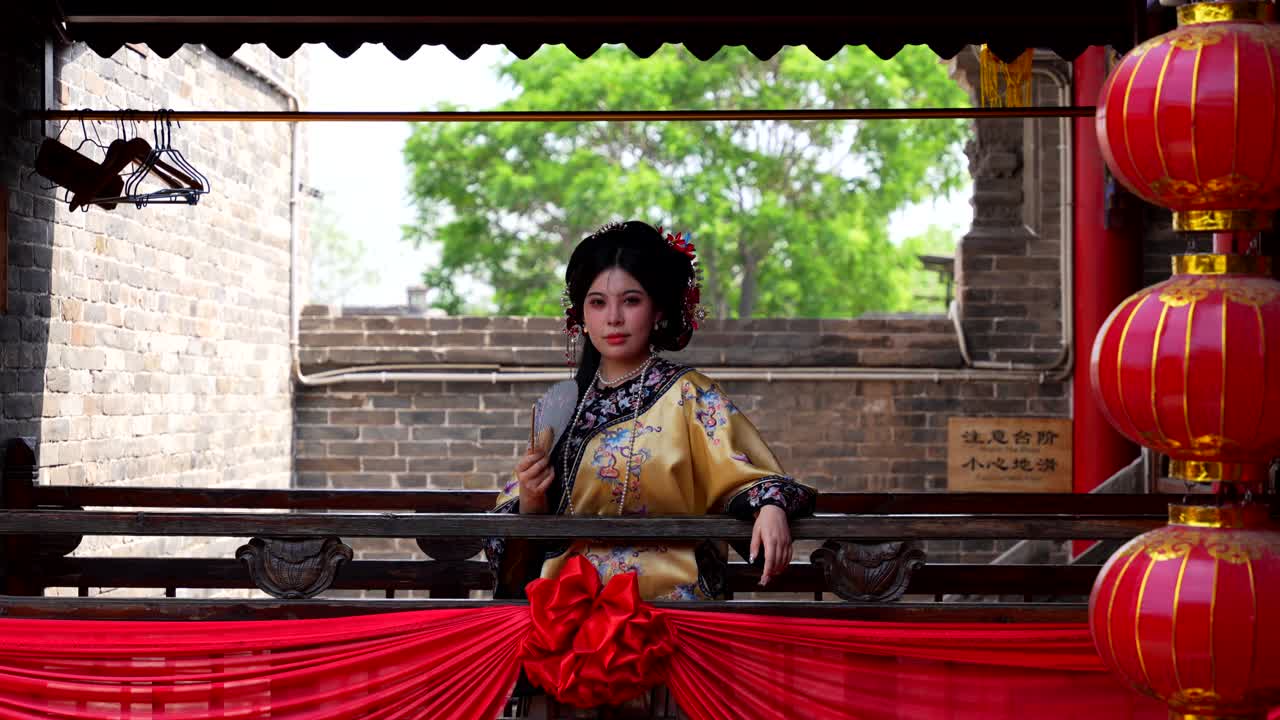 Woman dressed in traditional Qing Dynasty clothing smiles at camera while using a hand fan, China