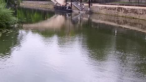 Drone-view-flying-forward-above-the-calm-water-surface-of-a-city-canal-in-Bath,-UK