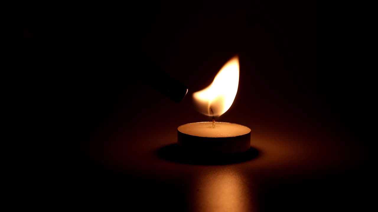A close-up view of a candle flame flickering gently in a dark setting, casting a warm glow.