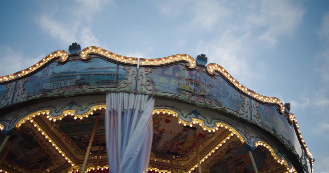 4K cinematic close-up of a spinning carousel at dusk against a blue evening sky. A colorful amusement ride creates a nostalgic fairground atmosphere with gentle motion, at San Francisco Pier 39.