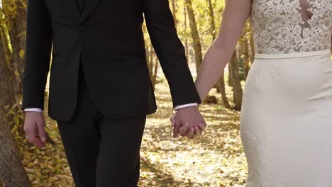 bride and groom holding hands walking through autumn woods