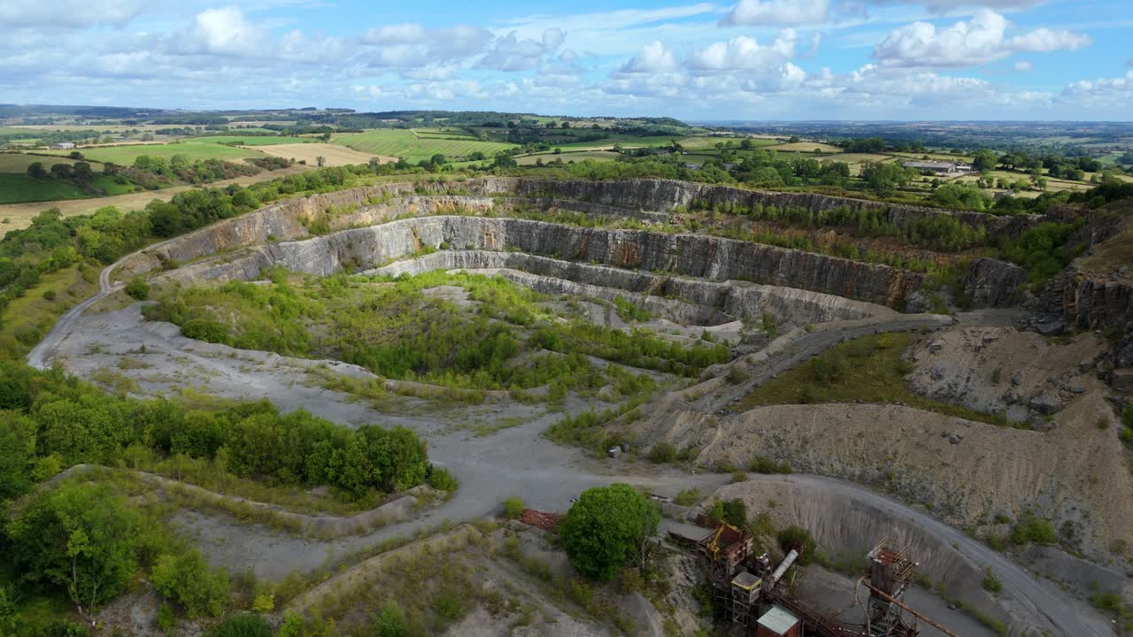 Aerial drone orbit around Crich Quarry revealing limestone extraction area with cliffs and green fields in the Derbyshire Dales