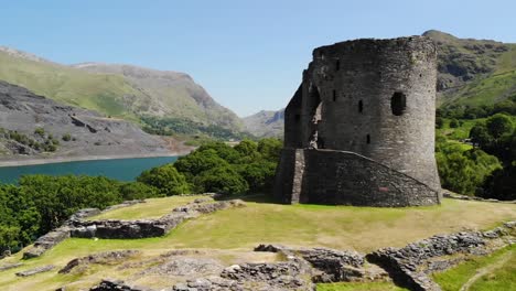 aerial shot of castle ruins in wales with the beautiful countryside in the background including a lake, rolling hills, and trees