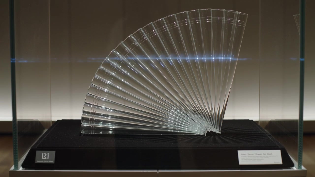 Shifting overhead light causing clear fan sculpture fanning blades in case, black base, placards