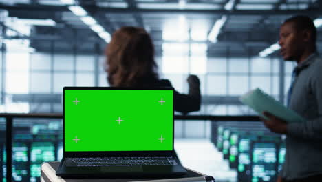 laptop de pantalla verde frente a los ingenieros del centro de datos inspeccionando los servidores
