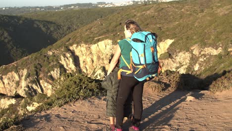 mamá con mochilas de camping y hija niño de pie en el acantilado