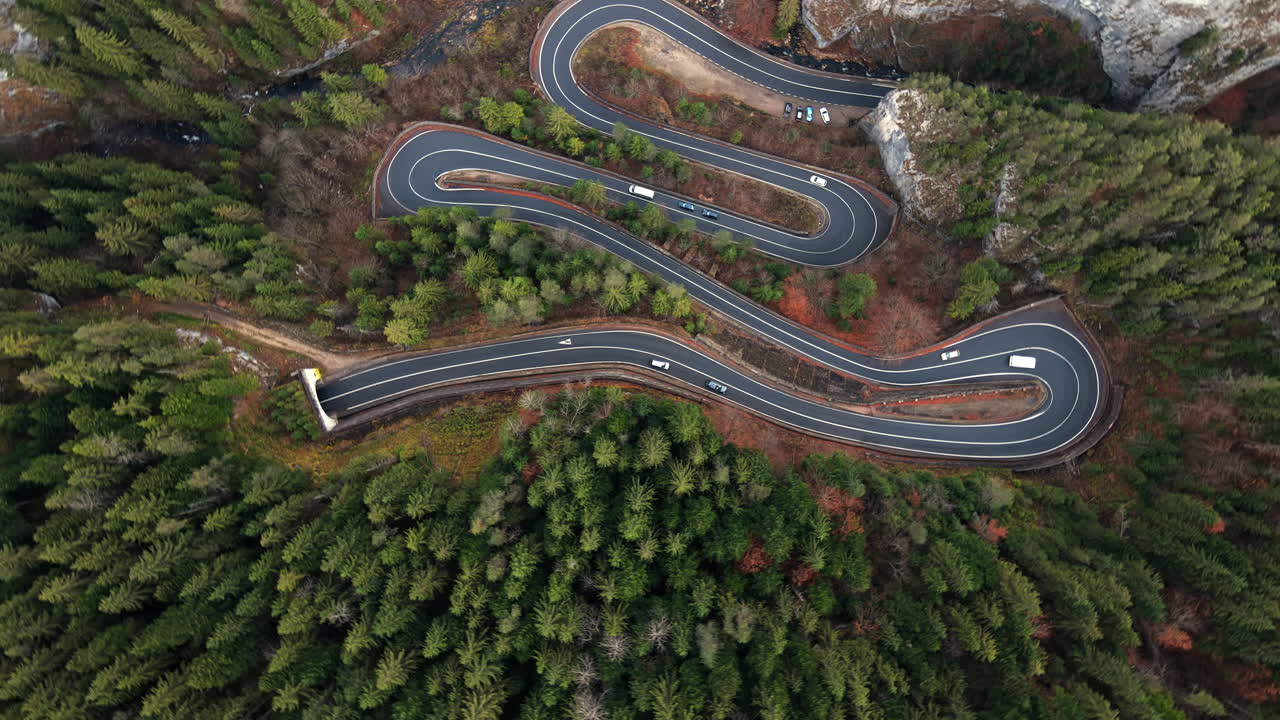 Aerial drone view of nature in Romania. Carpathian mountains, serpentine road with cars in the valley, rocky hills covered with lush forest