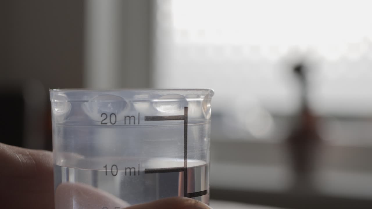 A man pours medicine into a measuring cup. Close-up.