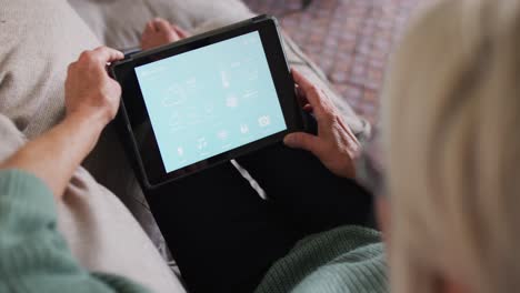 Happy-senior-caucasian-woman-sitting-on-sofa-in-living-room,-using-tablet