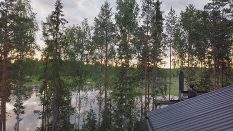 Woman-enjoys-landscape-on-Summer-cabin-balcony-surrounded-by-forest-trees,-aerial