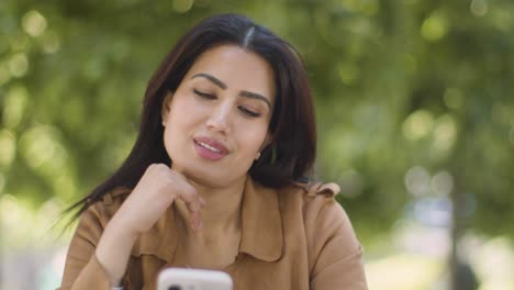 Muslim-Woman-Sitting-At-Outdoor-Table-On-City-Street-Sending-Text-Message-To-Date-On-Mobile-Phone