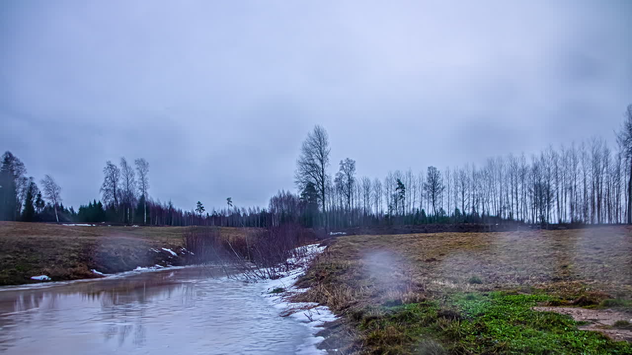 Aikaviivekuvaus jokivarsimetsän ja niittyalueen sulamisesta sateessa, aamunkoitosta keskipäivään.