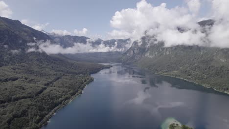 video con un dron de espalda plana sobre el lago bohinj avanzando hacia su interior entre las montañas, el cielo está despejado con algunas nubes