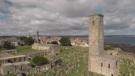 aerial drone flying by one of the towers of the st andrews cathedral as other towers and the coastline come into view in the background in st andrews, scotland, uk