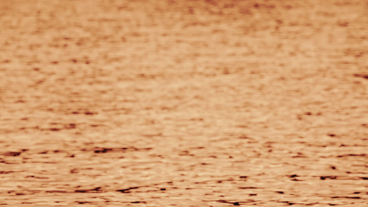 Close up of orange and gold sunset reflections moving across gentle water ripples