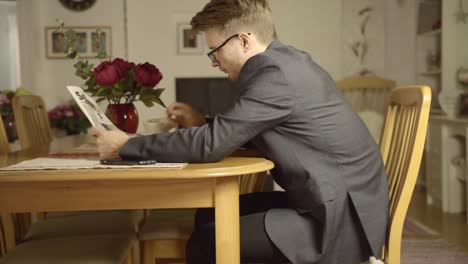 a young business man sits at a table wearing a suit and reads the newspaper