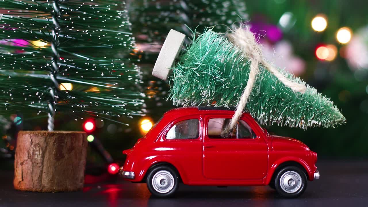 Auto d'epoca rossa che trasporta un albero di Natale sul tetto e luci intermittenti dietro