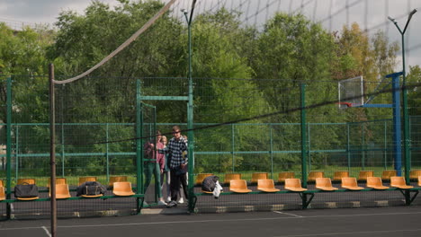 coach discussing strategy with young volleyball players on outdoor court, players listening attentively, preparing for warm-up run in sports attire against green backdrop