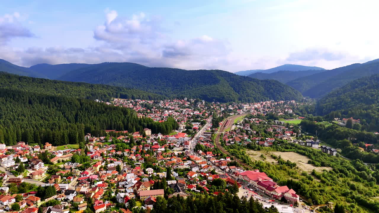 Sorvolo del paesaggio urbano soleggiato della verde e accogliente città situata nella zona montuosa. Montagne verdeggianti intorno a Busteni, Romania