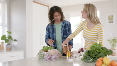 Happy diverse couple unpacking shopping bags in ktichen, slow motion