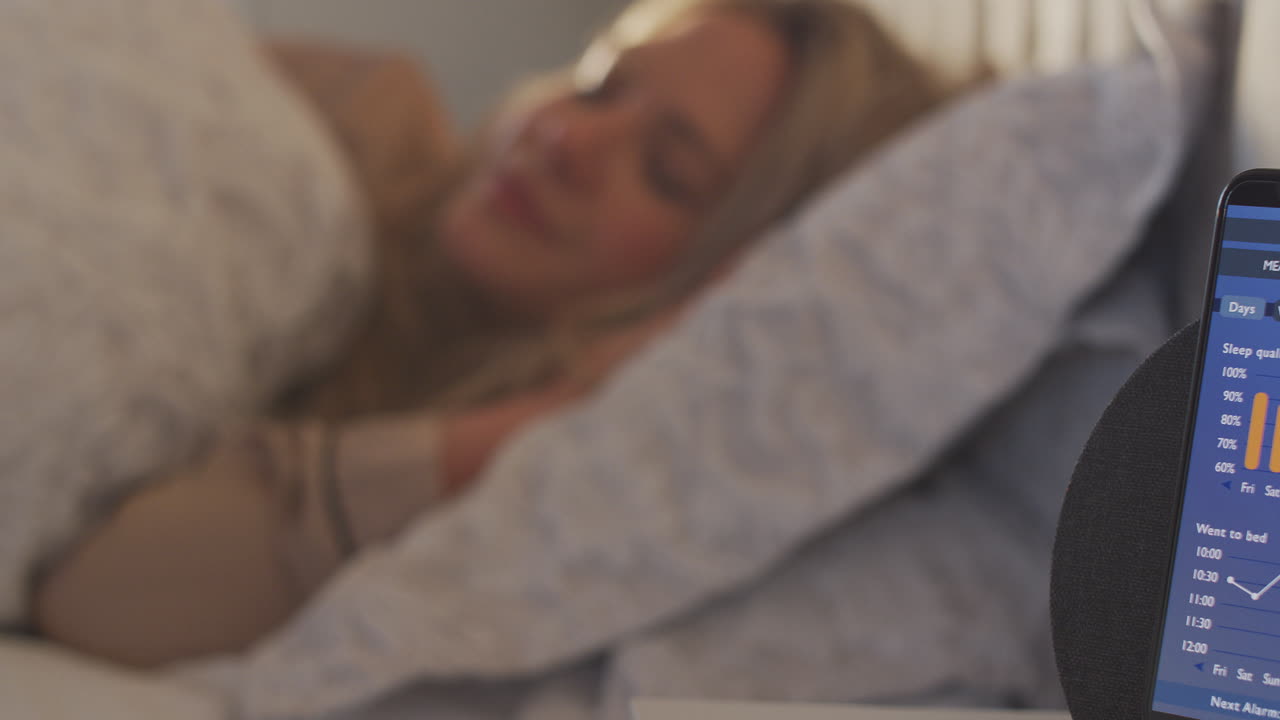 침대 에 휴대 전화로 실행되는 수면 데이터 앱으로 침대에서 잠자는 여성