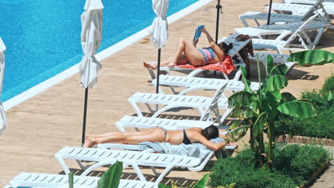 personas sentadas a la orilla de la piscina de un resort durante las vacaciones de verano