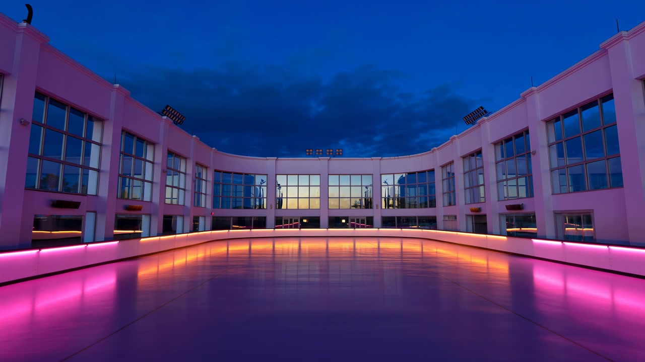 Centered view of a contemporary courtyard with reflective paving, illuminated glass facades, and pink accent lighting under a deep blue evening sky