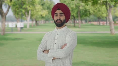 portrait of happy sikh indian man standing crossed hands in park