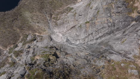 Aerial footage looking down a steep cliff before tilting up to showcase Matrefjellene peaks, valleys, and sunlit slopes in spring