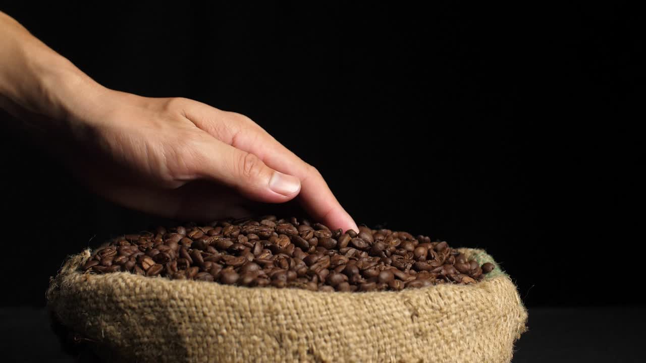 Hand Holding Coffee Beans And Pouring In Sack Bag On Dark Background, Slow Motion