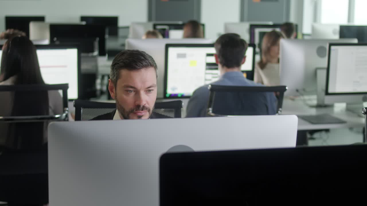 Portrett av middelaldrende mann på åpent kontorlandskap som jobber på stasjonær datamaskin. Mannlig profesjonell skriver på PC-tastatur. Portrett av positiv forretningsmann som ser på dataskjermen.