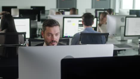 portrait of middle-aged man in open space office working on decktop computer. male professional typing on pc keyboard. portrait of positive business man looking at computer screen