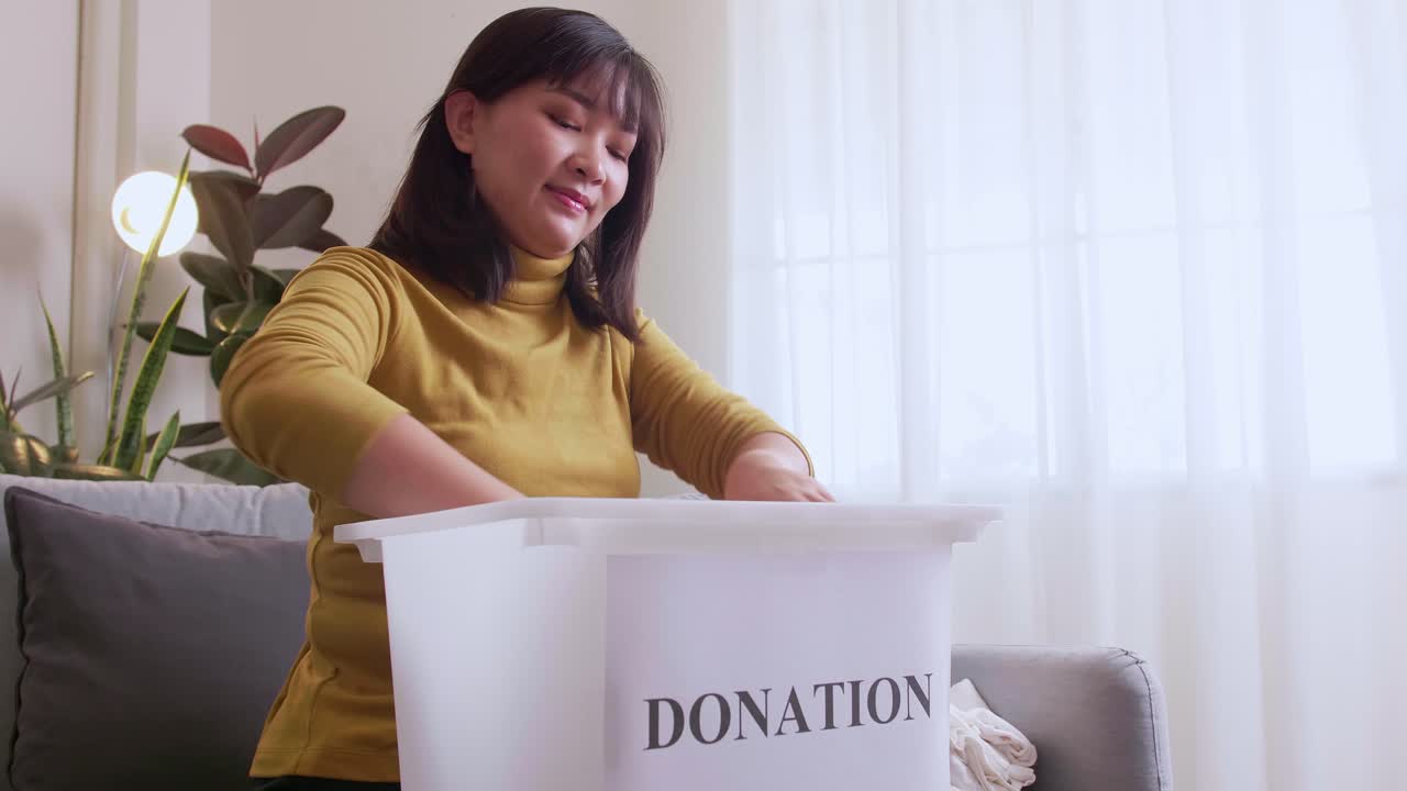 mujer asiática seleccionando ropa para donar y poniéndola en una caja