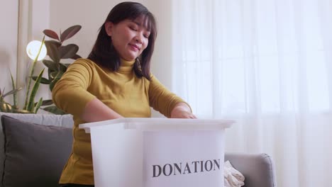 asian woman selecting clothes for donation and putting them in a box