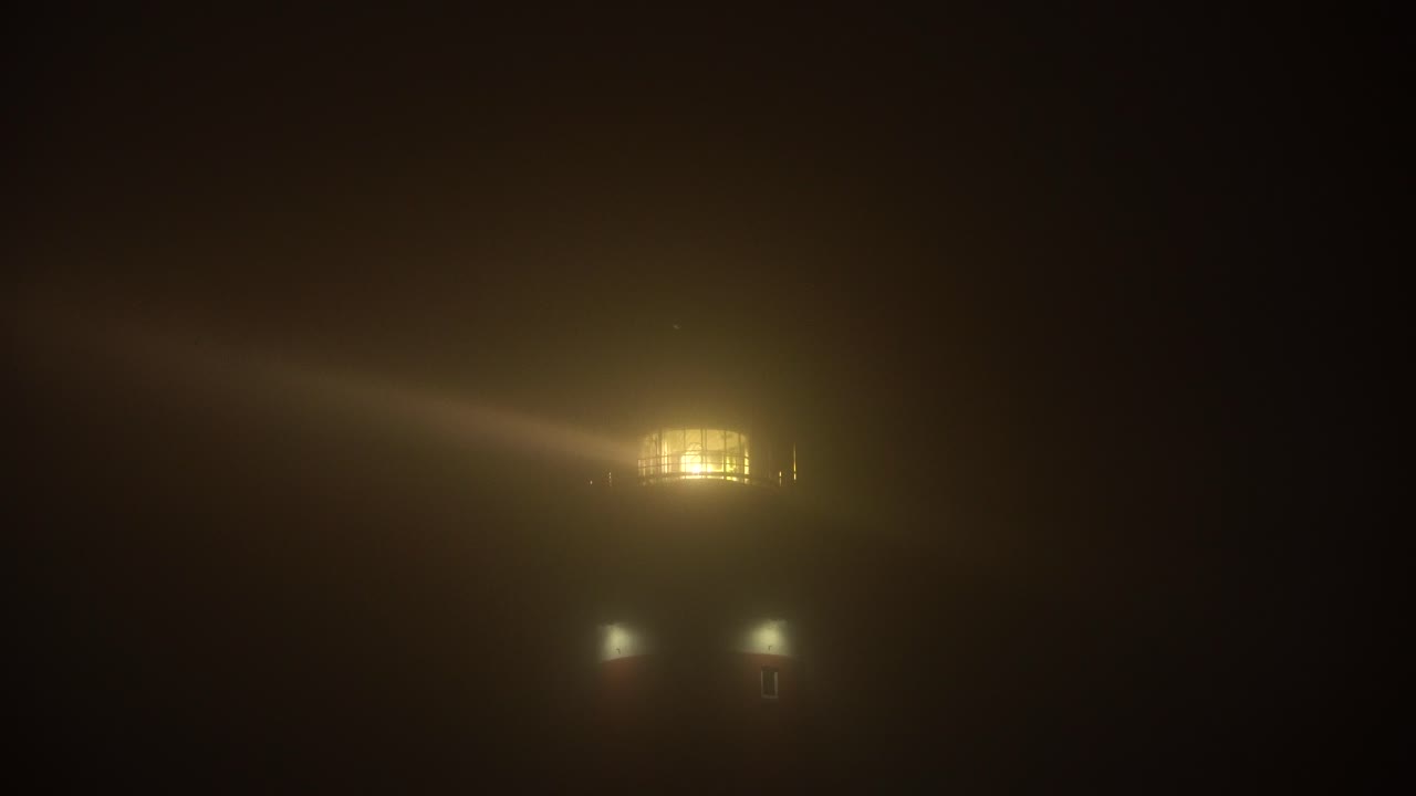 Lighthouse in dense fog with large beams penetrating through the mist