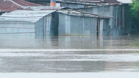 tin shed houses near the river become submerged in water during flood in bangladesh, south asia - pan right shot