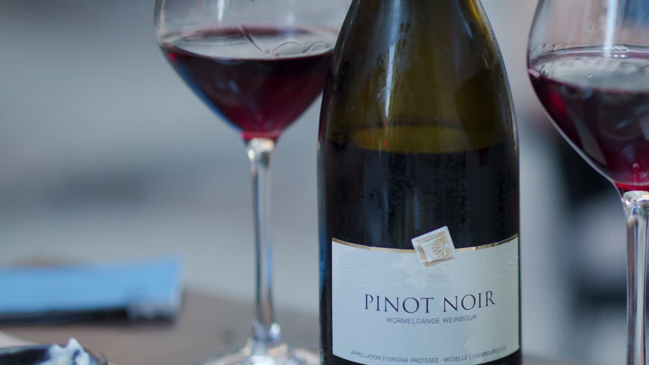 Pinot Noir bottle and filled glass on blurred outdoor table, soft daylight, subtle movement