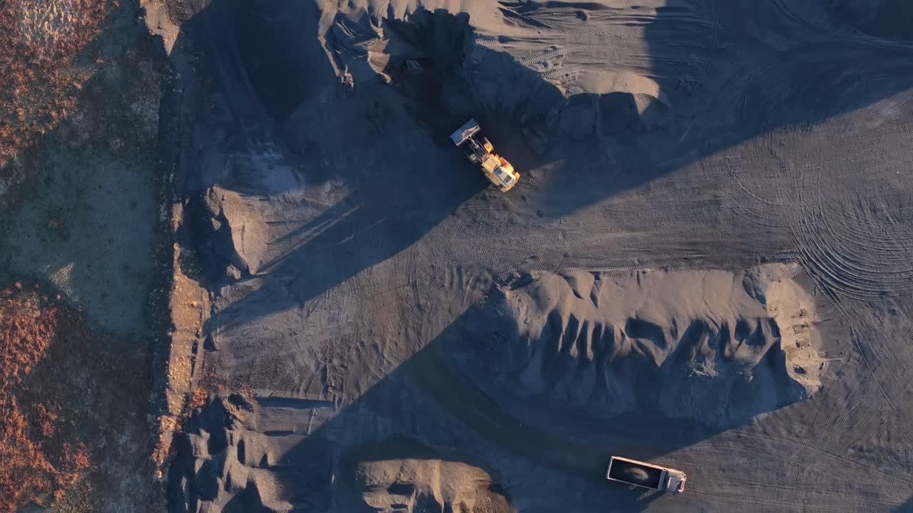 Drone perspective of rugged quarry terrain with trucks under warm evening glow