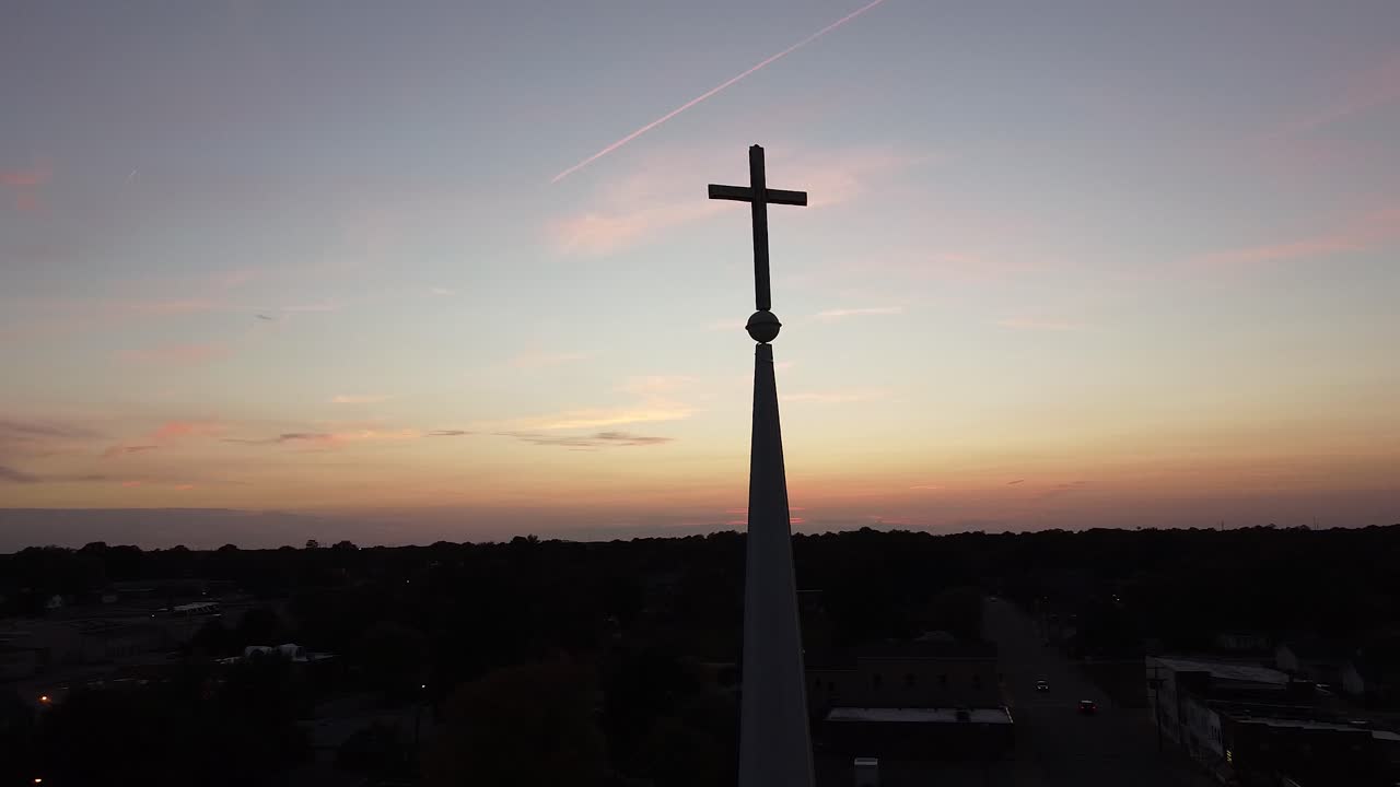 Drone orbit around cross on a church steeple with a gorgeous sunset over the city skyline.