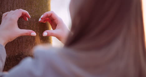 woman make heart shape with hands in forest