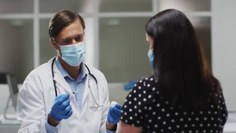 médico masculino caucásico con máscara facial dando vacunación a una paciente femenina