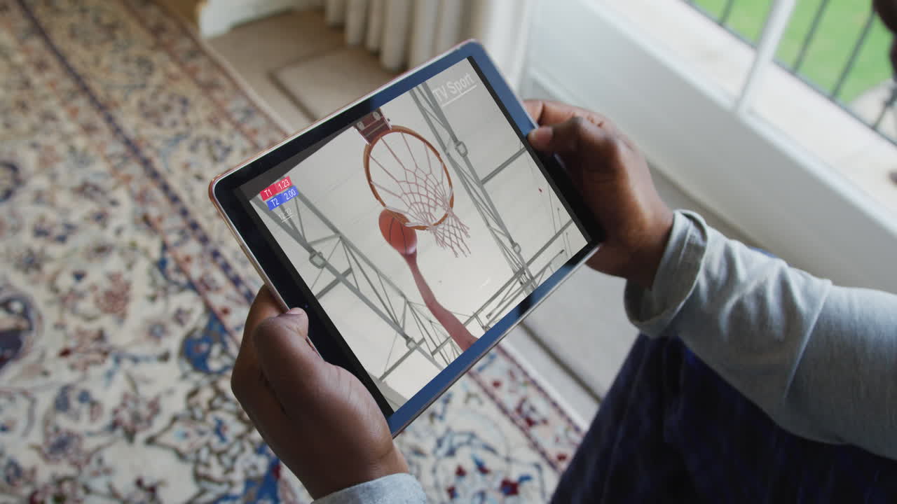 compuesto de un hombre sentado en casa viendo baloncesto en la tableta