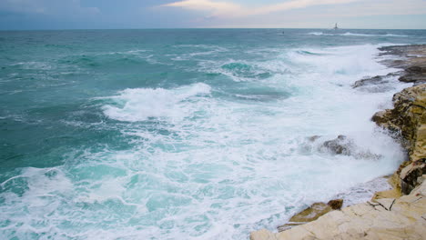 Big-sea-waves-crushing-on-rocky-shore,-lighthouse-Porer-and-cardinal-mark-on-restless-sea