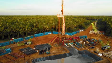 imágenes cinematográficas de drones de 4k de la estructura del equipo de la plataforma de perforación en tierra para la exploración y explotación de petróleo en medio de la jungla rodeada de palmeras durante la puesta de sol y el alto precio del petróleo