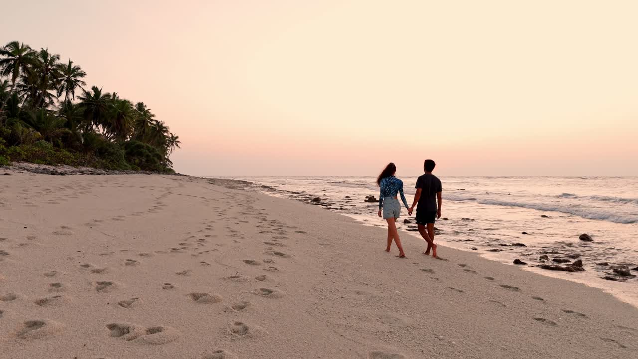 A romantic aerial drone shot captures a couple enjoying a quiet moment on Geiymiskih Fannu Beach at sunset in Fuvahmulah, Maldives.