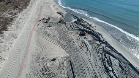 Drohnenaufnahme-Von-Strandnahrung-Oder-Das-Hinzufügen-Von-Sand-Oder-Sedimenten-Zu-Stränden-Zur-Bekämpfung-Der-Erosion,-Wobei-Wasser-Aus-Dem-Rohr-Austritt